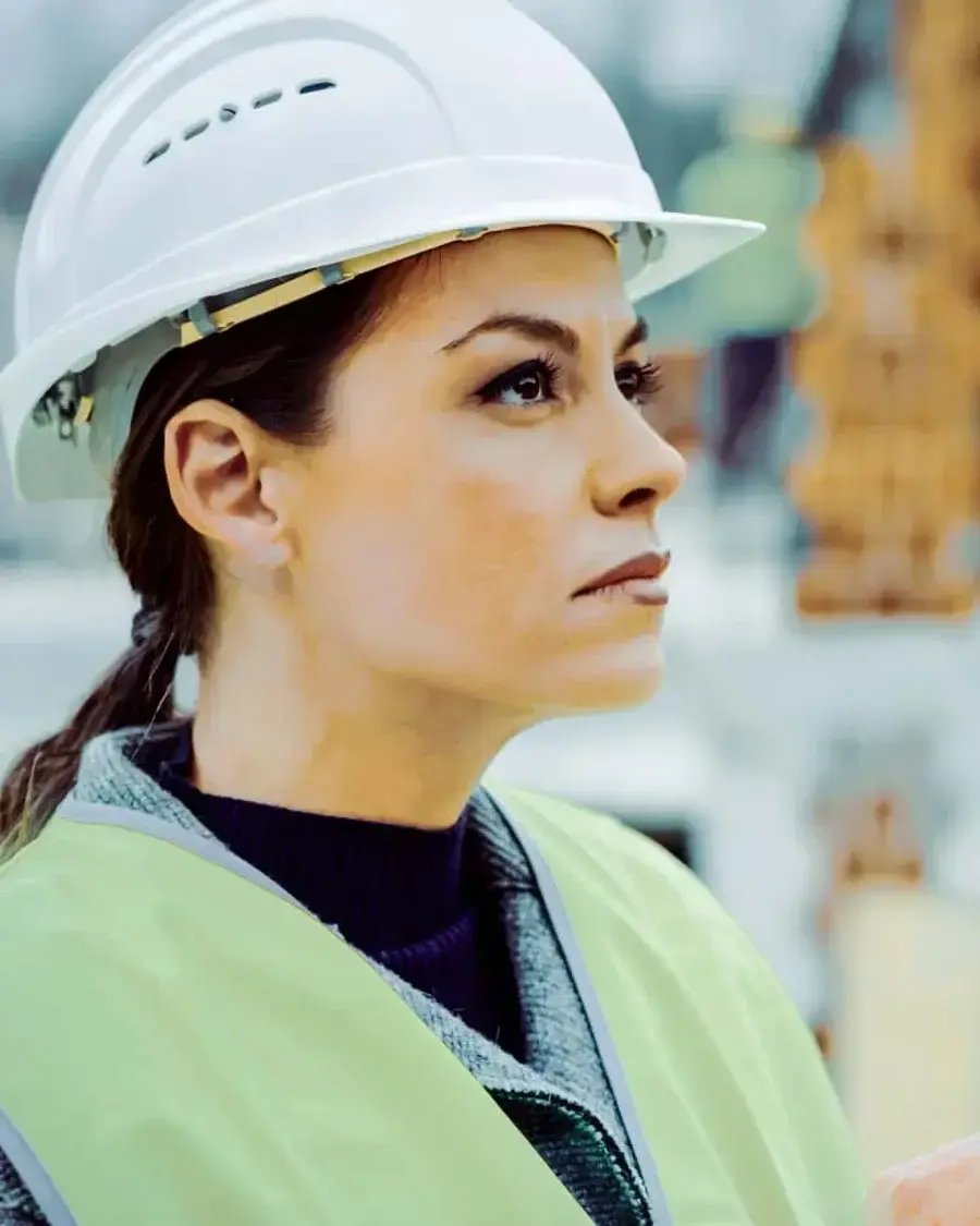 A close up of a woman in a hard hat looking up at a construction project