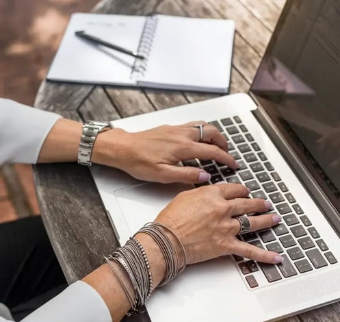 hands on computer with notepad to left