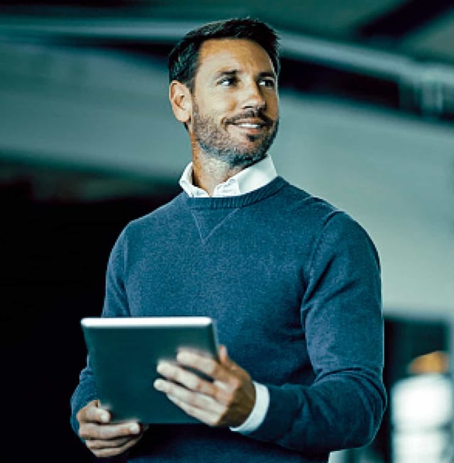 A smiling man looks off-camera while holding a tablet.