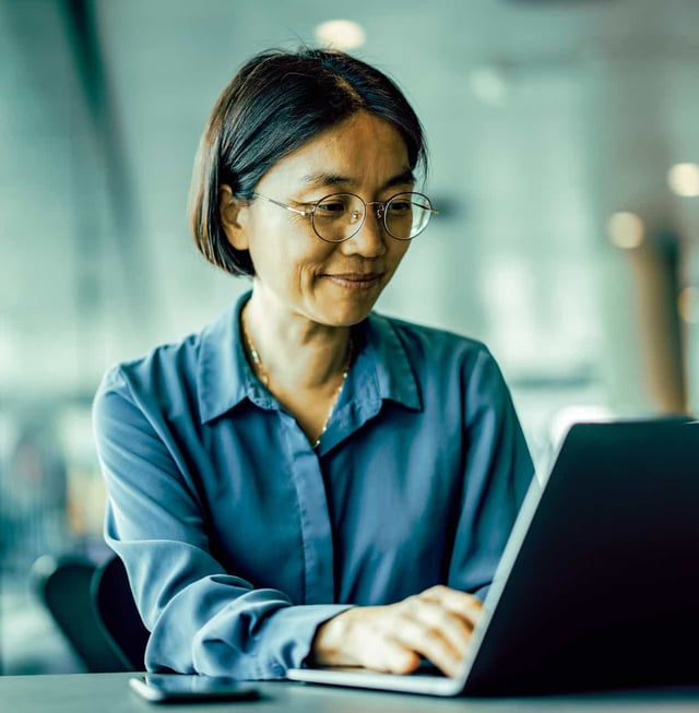 A woman sits typing on a laptop in an open office area.