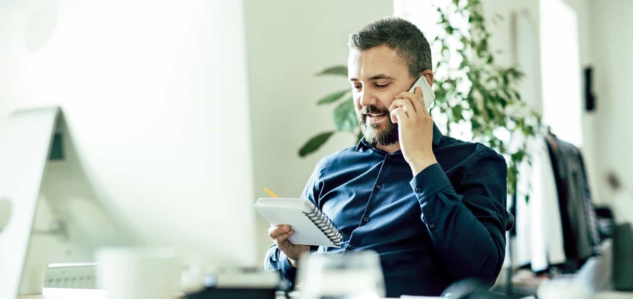 Man speaking on the phone while reviewing a notebook. 