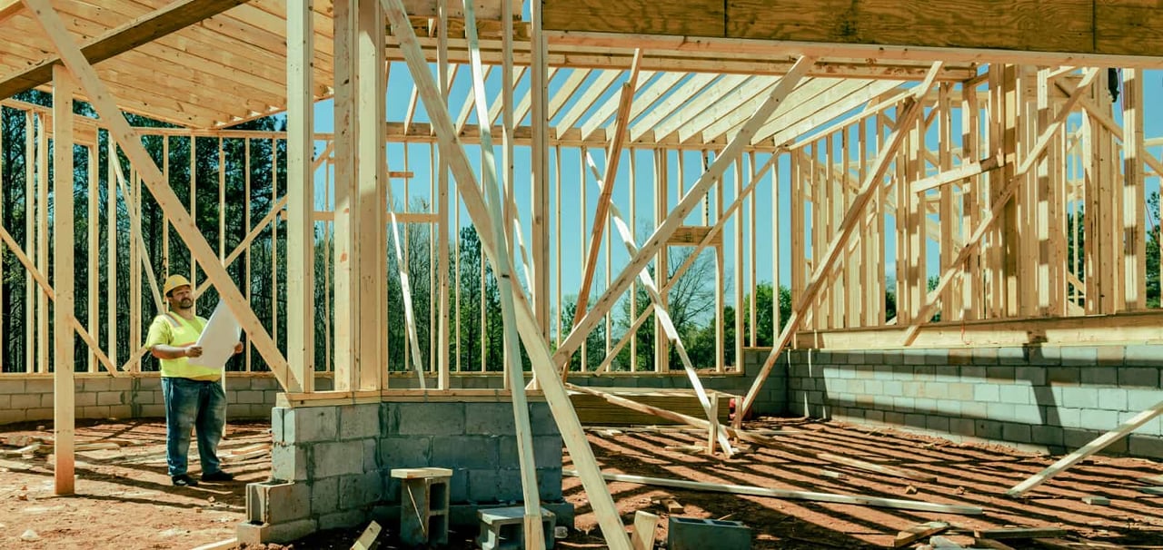 A construction worker looks at plans in a partially-constructed building.