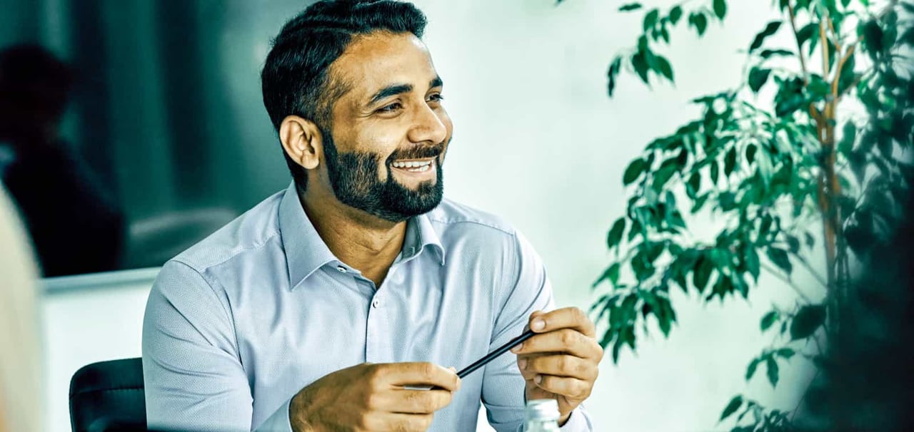 A smiling man fiddles with a pen while sitting at a conference table.