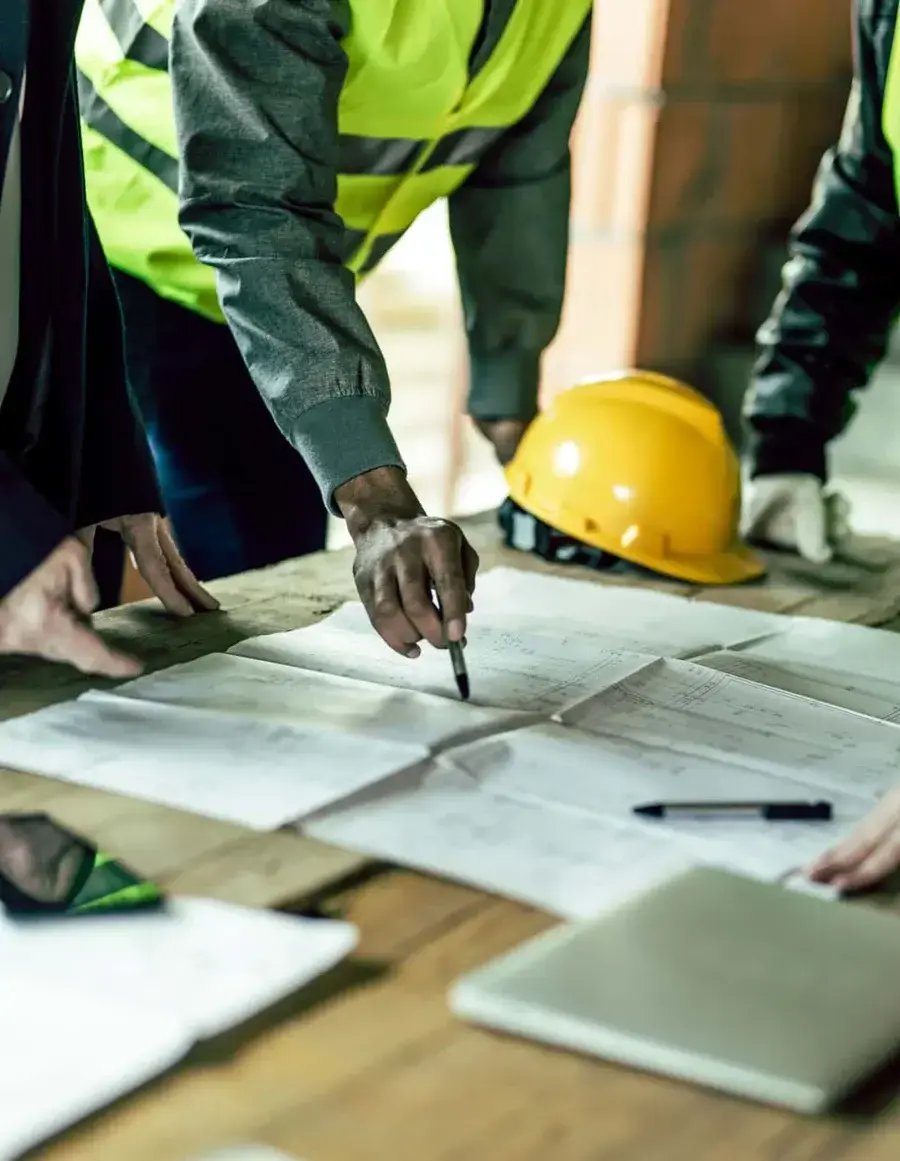 A group of people review plans on a wooden table at a construction site