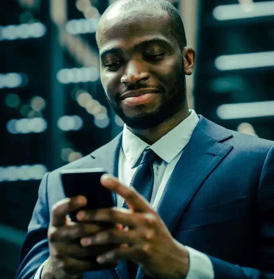 A businessman in a suit smiles while typing on his smartphone