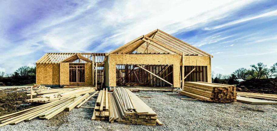 Stacks of lumber in front of a single family home in the process of being built.