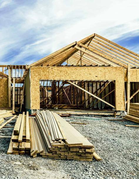 A construction site with a pile of boards in front of a partially-framed house